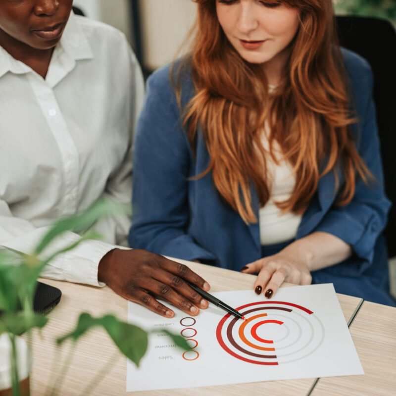 Focus on a diverse woman hands pointing on charts on a desk Multiracial colleagues working on their project and looking at documents in an office. Business professionals meeting in office. Focus on a diverse woman hands pointing on charts on a desk.